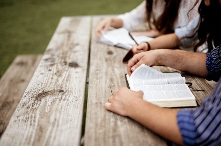 A closeup shot of people sitting near each other and reading the bible with a blurred background